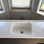 Бесшовная угловая столешница с мойкой и пристенным плинтусом на кухню из искусственного камня изготовлено в правила камня