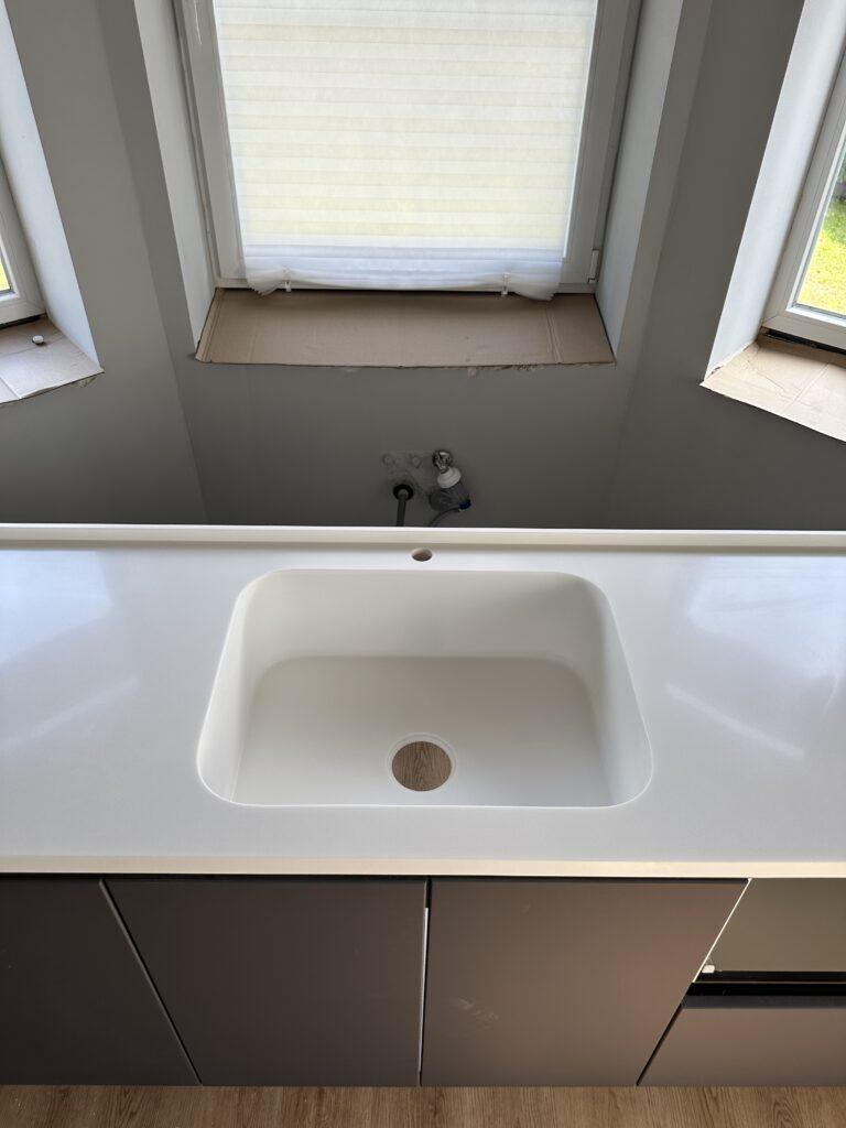 Бесшовная угловая столешница с мойкой и пристенным плинтусом на кухню из искусственного камня изготовлено в правила камня